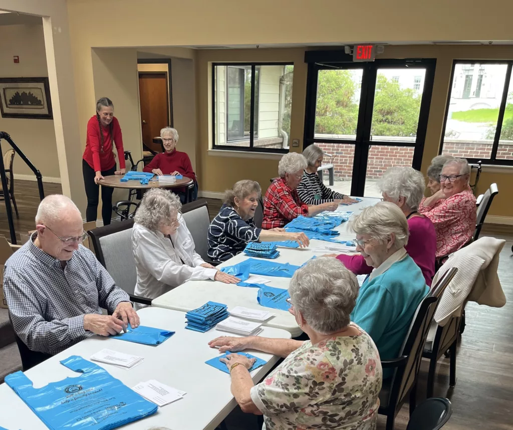 Several Terrace residents sitting down stuffing donation envelopes into shopping bags for volunteered for the National Association of Letter Carriers Stamp Out Hunger National Food Drive