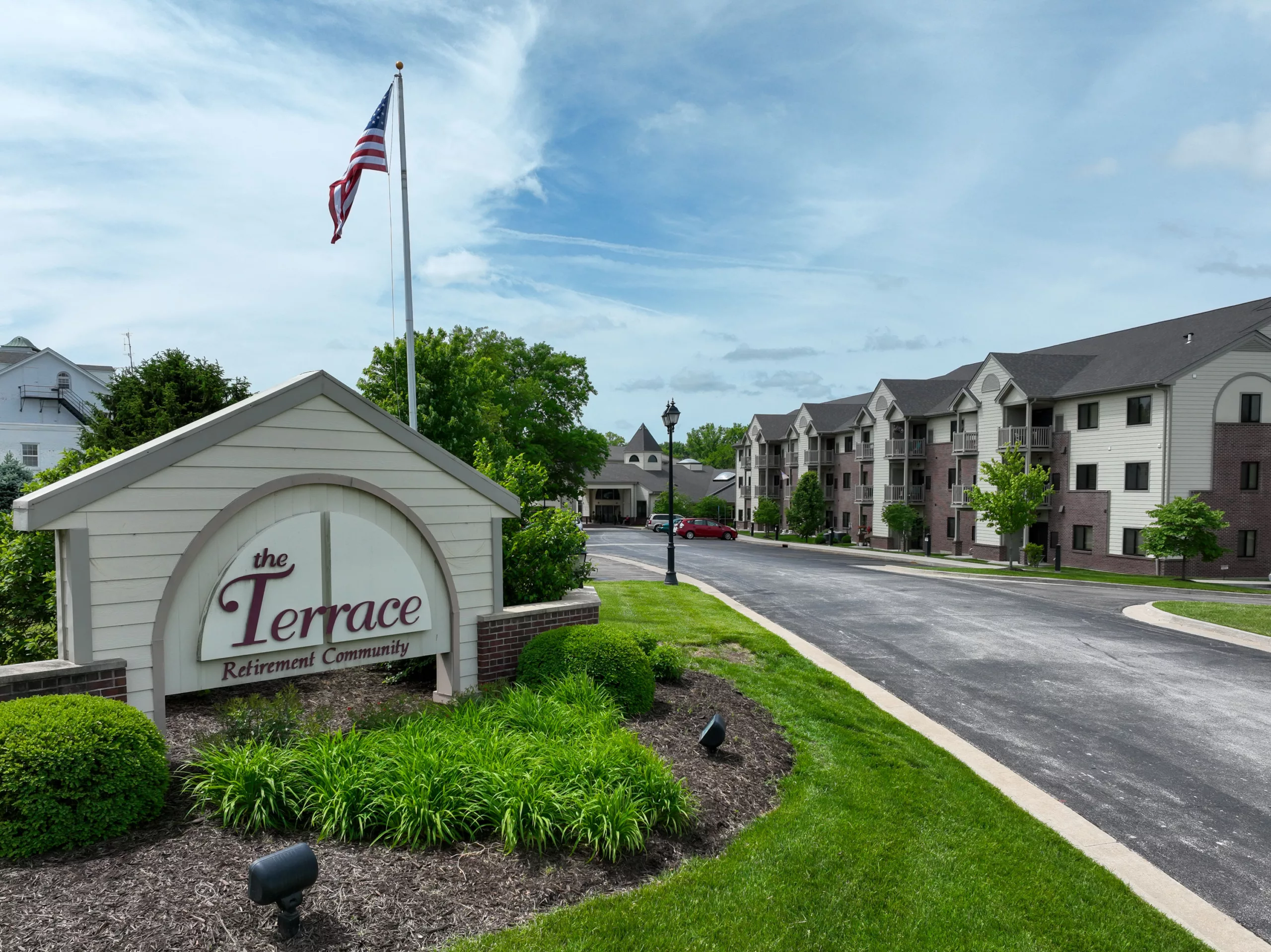 The Terrace Retirement Community entrance sign with an American Flag behind it and the senior apartments.