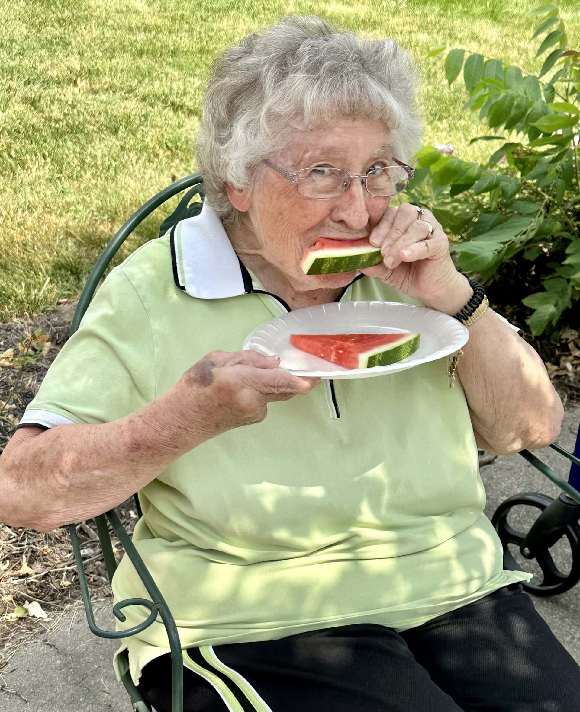 senior lady outside sitting outside in the Terrace Courtyard taking a bite of watermelon