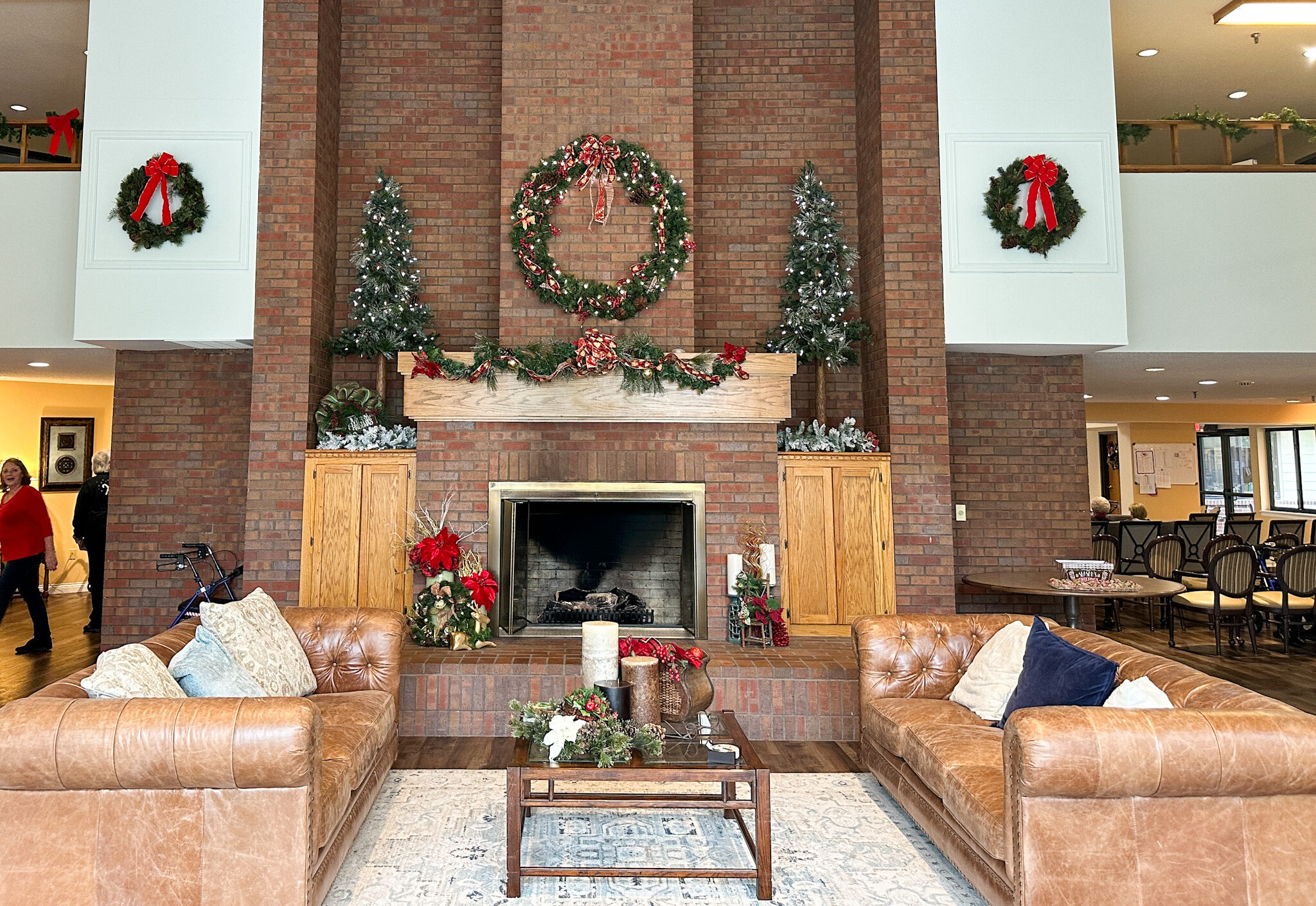 A large brick fireplace with Christmas wreaths on each side with two couches and a table in front of it